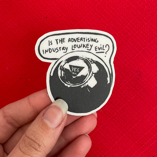 A hand holding a die-cut sticker with a black and white 8-ball illustration and the text 'IS THE ADVERTISING INDUSTRY LOWKEY EVIL?' against a bright red textured background. The 8-ball says "Yes."