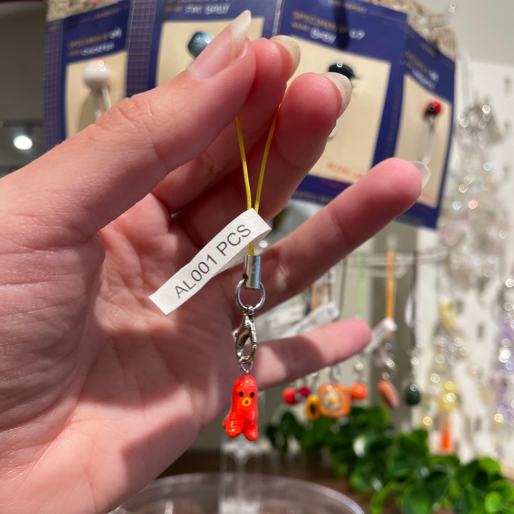 A hand holds a small sausage octopus charm with a yellow loop strap and a white paper tag.